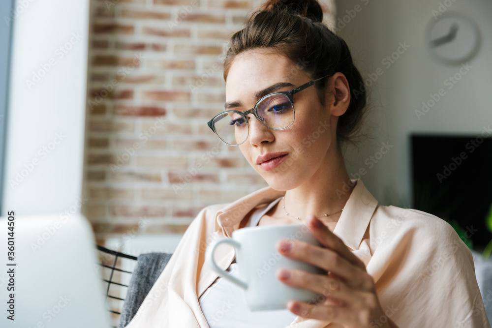 © Drobot Dean - Image of woman working with laptop and drinking coffee while sitting © Drobot Dean - Image of woman working with laptop and drinking coffee while sitting