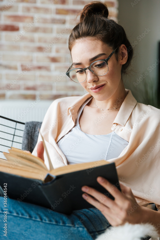 Image of pleased nice woman wearing eyeglasses reading book Image of pleased nice woman wearing eyeglasses reading book