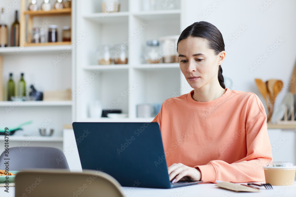 Young woman using laptop computer at her work while sitting at the table in the kitchen Young woman using laptop computer at her work while sitting at the table in the kitchen