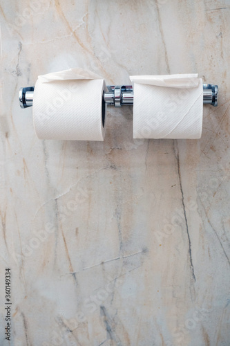 Two white toilet rolls on a modern metal hanger, Light marble tile wall. House hold object.