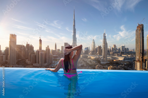 Beautiful young woman enjoys the panoramic view from an infinity pool on downtown Dubai