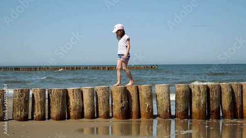 Little kid girl walks on wooden pier on Baltic sea beash near shallow waterline summer rest during vacations photo