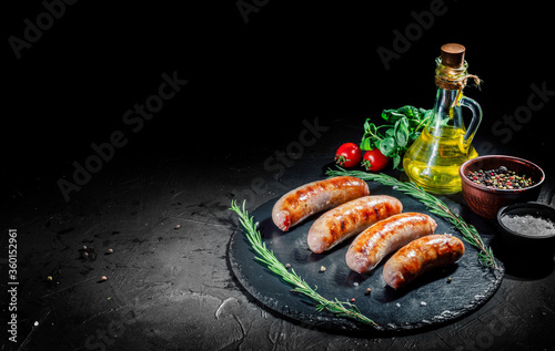Foto Grilled sausage with the addition of herbs and vegetables on a dark background