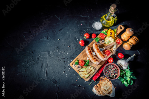 Grilled sausage with the addition of herbs and vegetables on a dark background © Andrii