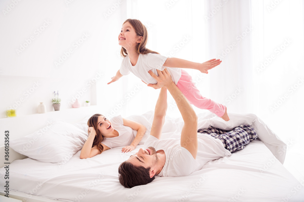 Photo of young happy family lady mommy guy daddy hold arms little girl daughter raise up lying sheets having fun good mood spend together quarantine weekend bedroom indoors Photo of young happy family lady mommy guy daddy hold arms little girl daughter raise up lying sheets having fun good mood spend together quarantine weekend bedroom indoors
