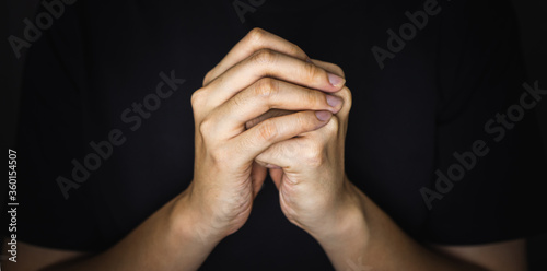 Praying hands of young man in the shadow.
