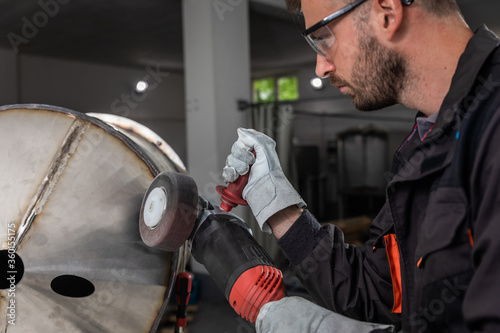 Industrial worker with angle grinder working and polishing metal structure at workshop.