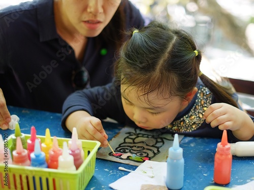 A Asian mother is teaching her young daughter to do an art project using colorful acrylic paints to draw an owl. photo