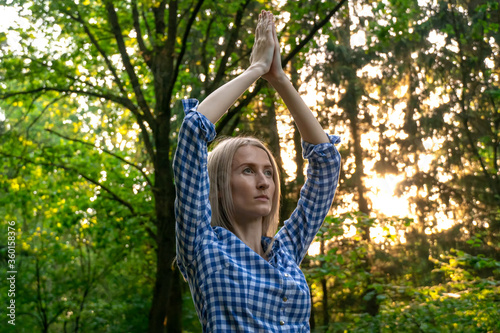 young beautiful blonde woman holding her hands above her head is playing sports in the forest at sunset. concept of yoga.