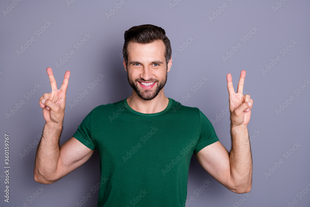 Photo of attractive handsome bearded guy raise hands showing v-sign symbols fingers saying hi to friends wear casual green t-shirt isolated grey color background Photo of attractive handsome bearded guy raise hands showing v-sign symbols fingers saying hi to friends wear casual green t-shirt isolated grey color background