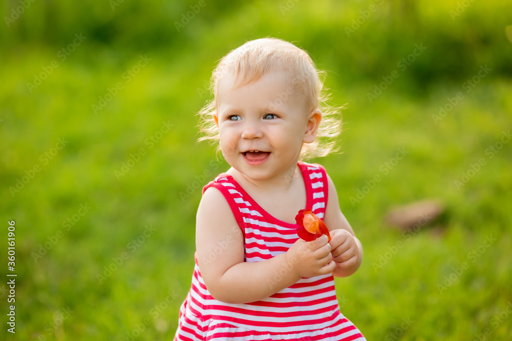 Cute little girl smiling in red summer dress walking on green lawn Cute little girl smiling in red summer dress walking on green lawn
