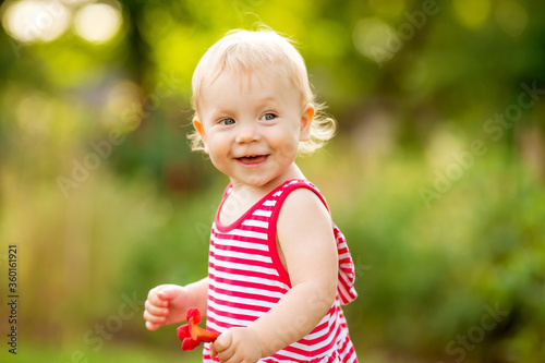 Cute little girl smiling in red summer dress walking on green lawn