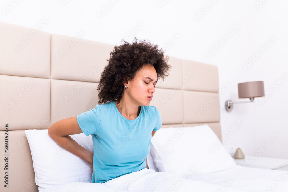 Hurt african American young woman sit in white bed wake up touch back suffering from painful backache, unwell black millennial girl awake from sleep having strong spinal muscular spasm strain Hurt african American young woman sit in white bed wake up touch back suffering from painful backache, unwell black millennial girl awake from sleep having strong spinal muscular spasm strain