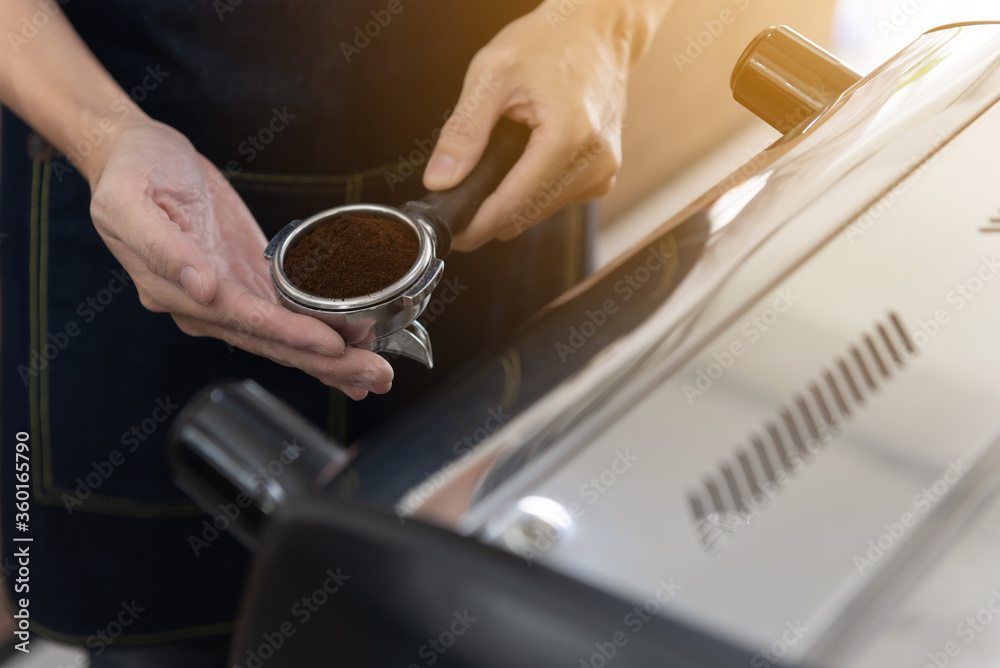 Hand of barista man holding coffee tamper with grind coffee for making coffee for customers. Closeup