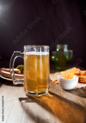 A mug of light beer on a dark background with snacks. Close-up