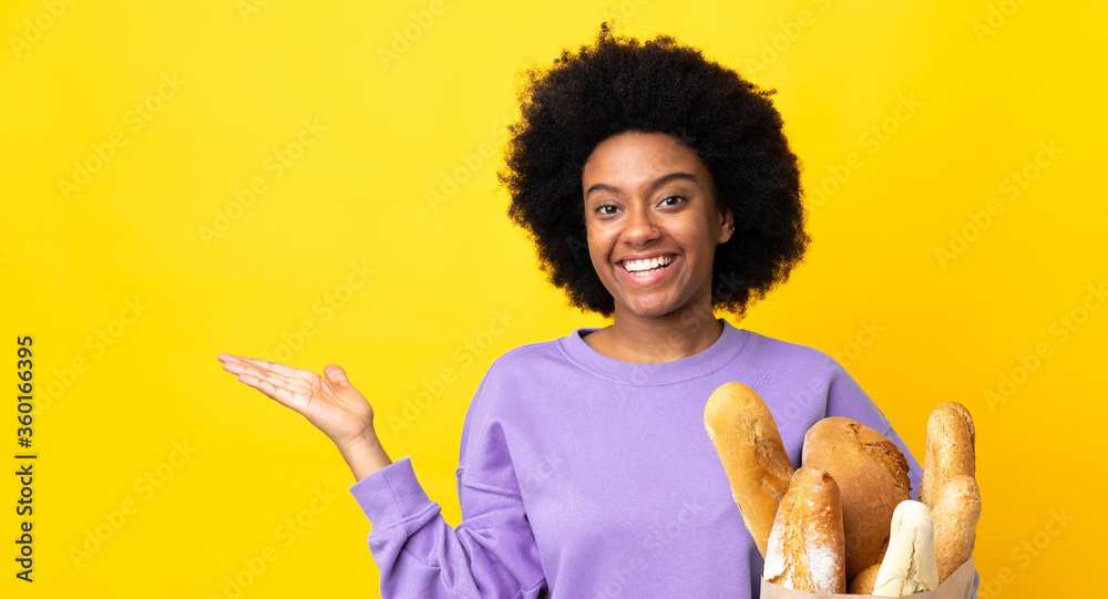 Young African American woman buying something bread isolated on yellow background holding copyspace imaginary on the palm to insert an ad