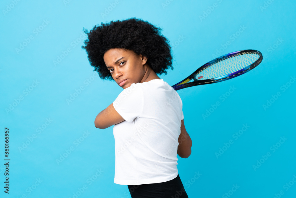 Young African American woman isolated on blue background playing tennis Young African American woman isolated on blue background playing tennis