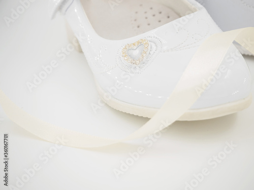 Pair of white baby lacquered girls shoes with beige ribbon at white background with place for text