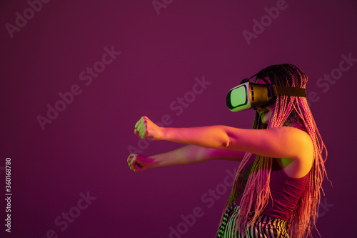 Playing emotional. Showing blank space, riding. Young woman on pink studio background in neon. Beautiful model with VR-headset. Human emotions, facial expression, sales, ad concept. Freak's culture. © master1305