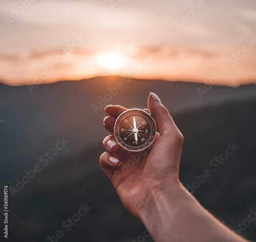 Woman hand with magnetic compass in summer mountains at sunrise, pov.