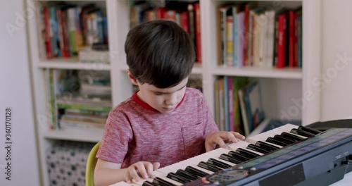 Preschooler child devotedly playing on electronic keyboard. 5 year old boy sitting behind table and enjoying playing on music keyboard while closing his eyes. photo