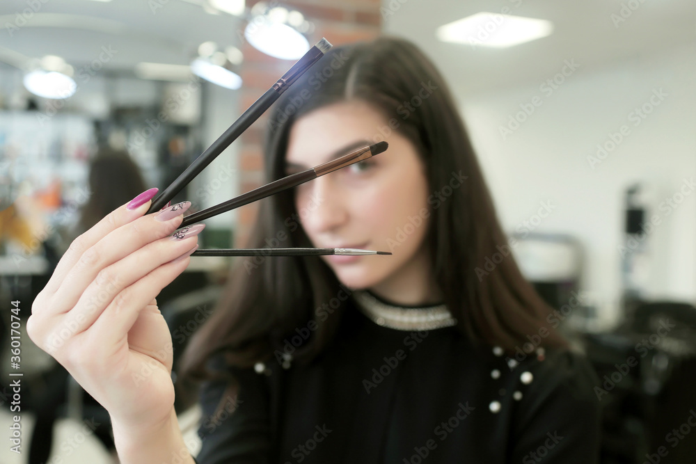Beautician with a special tool for eyebrows in a beauty salon. Beautiful woman eyelash master holds in her hand tweezers, tools for the care of eyelashes and eyebrows. Eyelash extension procedure.
