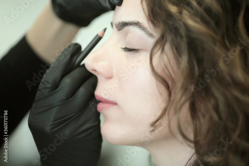 Eyebrow master colors eyebrows, doing permanent makeup. Woman doing makeup while working in black gloves in a beauty salon. Eyebrow concept. Close up portrait. Girl face