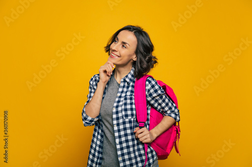 I wonder, what is waiting for me? A half-length photo of a young student, dressed casually, smiling, and wondering about her new day, holding her cute pink backpack on her one shoulder.