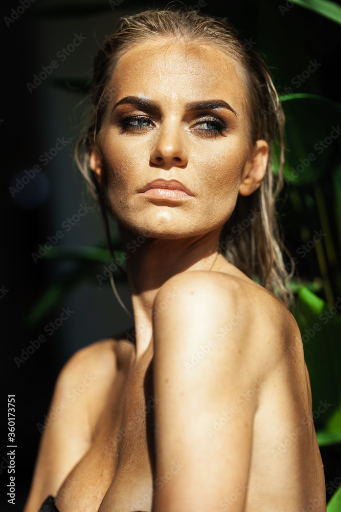 Relaxation and spa concept. Closeup portrait of a sexy fashionable lady in a black swimsuit. Woman with wet hair and makeup poses in green plants in swimming pool in natural sunlight Relaxation and spa concept. Closeup portrait of a sexy fashionable lady in a black swimsuit. Woman with wet hair and makeup poses in green plants in swimming pool in natural sunlight