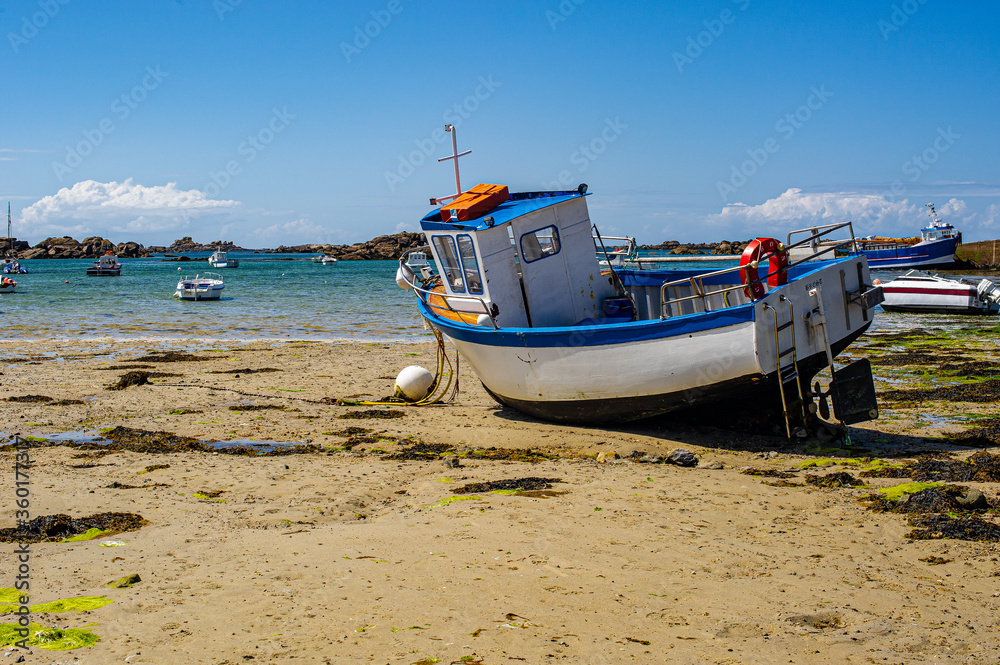Fishing boat on a beach in Brittany. Sandy beach strewn with seaweed.