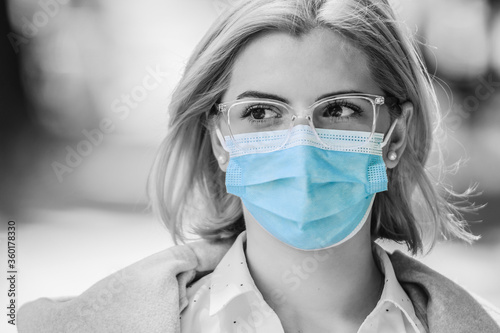 woman wearing medical face mask outside. black and white photo with only recommended pandemic prevention measures  in color to give focus on them