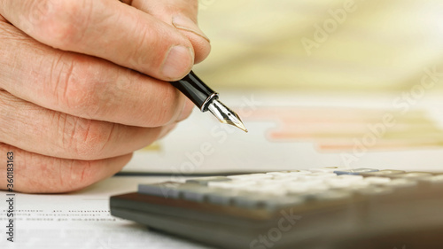 pensioner hand writes with fountain pen by calculator close