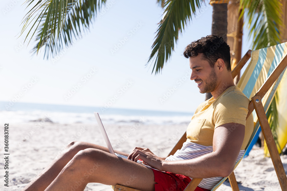 Caucasian man  sitting on a deck chair and using a laptop at the beach