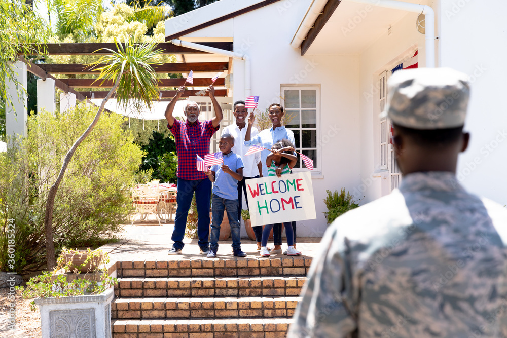 African American male soldier wearing uniform and his family standing by their house