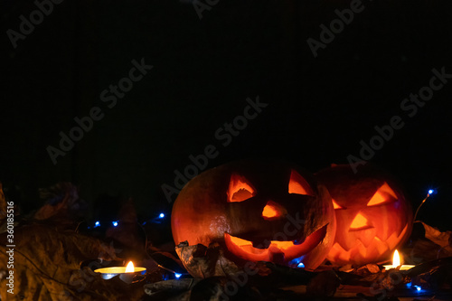 Two glowing pumpkins in the dark in the forest, candles lit around them, copy space. Beautiful background for Halloween.