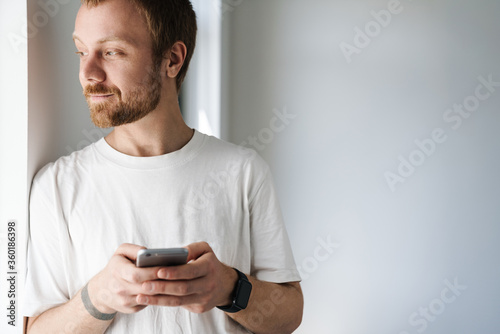 Photo of pleased bearded man using mobile phone while leaning on wall © Drobot Dean
