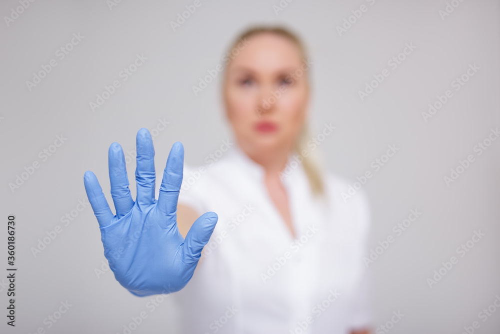 health care and corona virus pandemic concept - doctor in white uniform and blue gloves showing stop sign over gray health care and corona virus pandemic concept - doctor in white uniform and blue gloves showing stop sign over gray