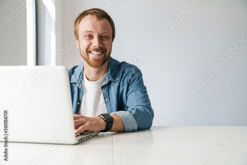 Photo of cheerful handsome man working on laptop while sitting at table