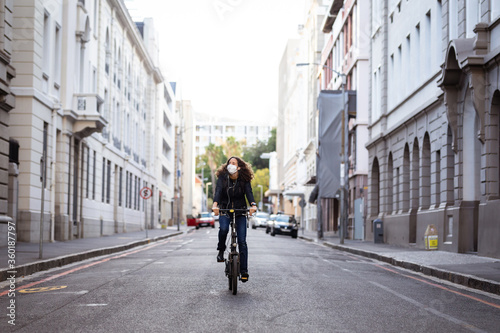 Caucasian woman wearing a protective mask and earphones, and biking in the streets © WavebreakMediaMicro