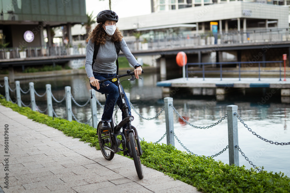 Fototapeta premium Caucasian woman wearing a protective mask and a cycling helmet in the streets, biking in the streets