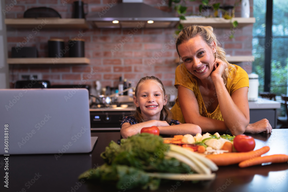 Caucasian woman and her daughter spending time in the kitchen and using a laptop