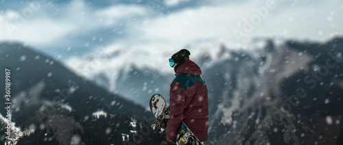 a skateboarder on top of mountains at the snow falling.