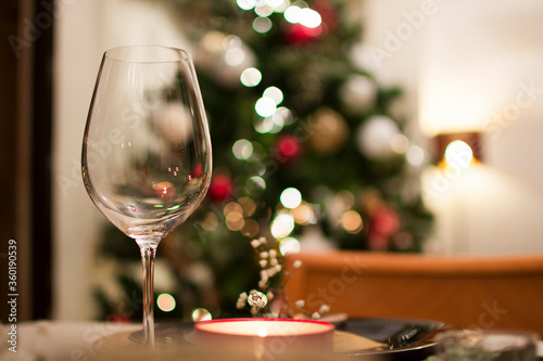 A crystal wine glass close-up on the table, with the bokeh of Christmas tree lights behind.