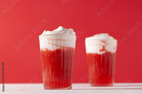 Quadro em tela Strawberry smoothie shakes in glass with whipping cream on red background