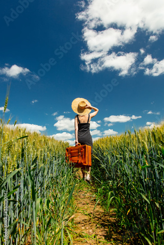 Beautiful blonde girl with suitcase in wheat field in sunny day