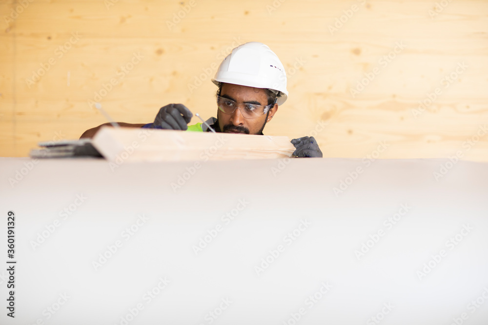 Junger Handwerker, Mann mit Helm, erstellt ein Holzgebäude Junger Handwerker, Mann mit Helm, erstellt ein Holzgebäude