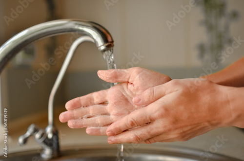  Washing hands with soap near the tap. Water pours from the tap.