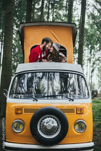 Traveler couple embracing and resting in forest on Orange retro Bulli Vintage Camper.