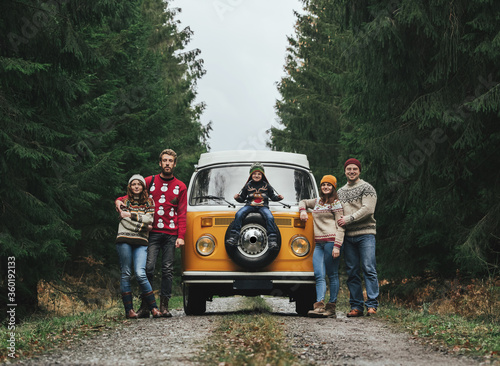 Group of young friends traveling by orange retro Bulli. Family vacation travel, holiday trip.