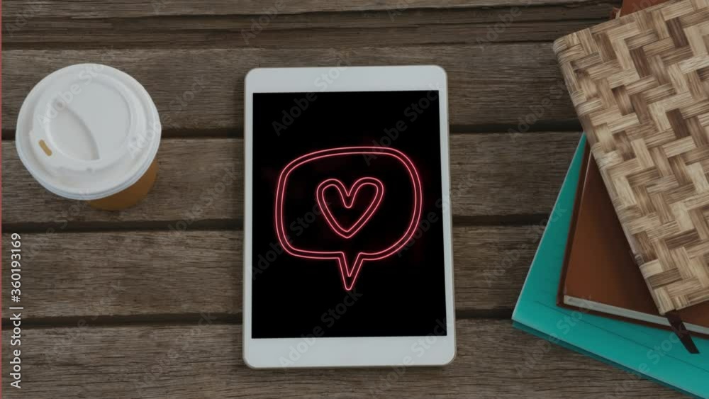 Animation of speech bubble with heart icon flickering on screen of digital tablet put on wooden desk Animation of speech bubble with heart icon flickering on screen of digital tablet put on wooden desk